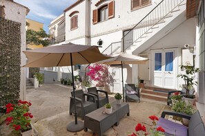 Une terrasse extérieure aménagée avec des meubles en osier, un grand parasol et des plantes en pot.
