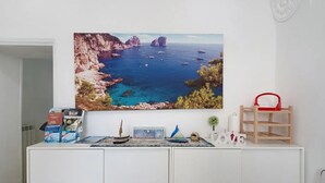 Une pièce décorée d’un grand tableau représentant un paysage côtier, d’une étagère en bois sur laquelle se trouve un panier rouge, et d’un meuble contenant divers objets.