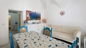 Une pièce comprenant une table à manger, des chaises, un canapé, un tableau, une horloge et donnant sur une salle de bain.