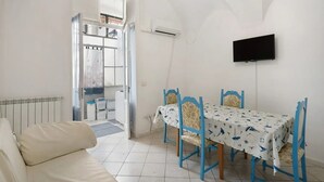Une pièce avec un radiateur blanc, un canapé, une table à manger avec des chaises bleues et un téléviseur fixé au mur.
