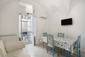 A room with a white radiator, a sofa, a dining table with blue chairs, and a TV mounted on the wall.