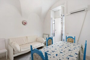Ein Zimmer mit einem weißen Sofa, einem Tisch mit einer Tischdecke im Seestil und einer Uhr an der Wand.