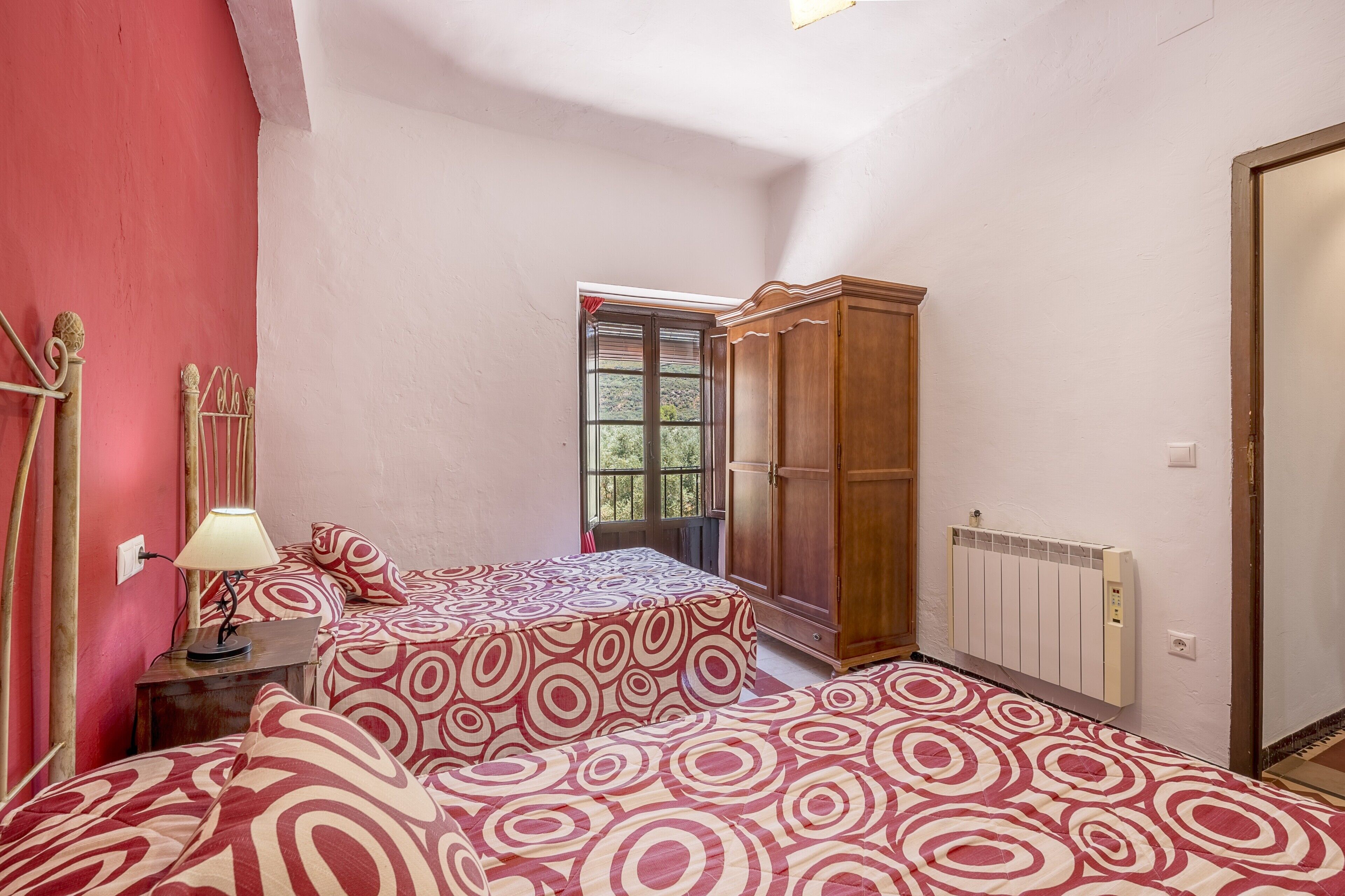 A bedroom with two beds, a wooden wardrobe, a radiator, and a window with a view.
