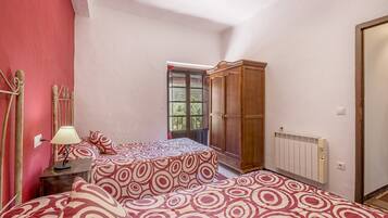 A bedroom with two beds, a wooden wardrobe, a radiator, and a window with a view.