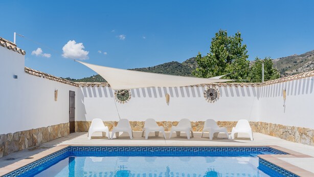Una piscina con sillas blancas, una pared blanca y vistas a las colinas.