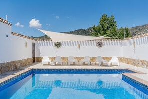Une piscine entourée de chaises blanches, avec un mur blanc et une vue sur des collines.