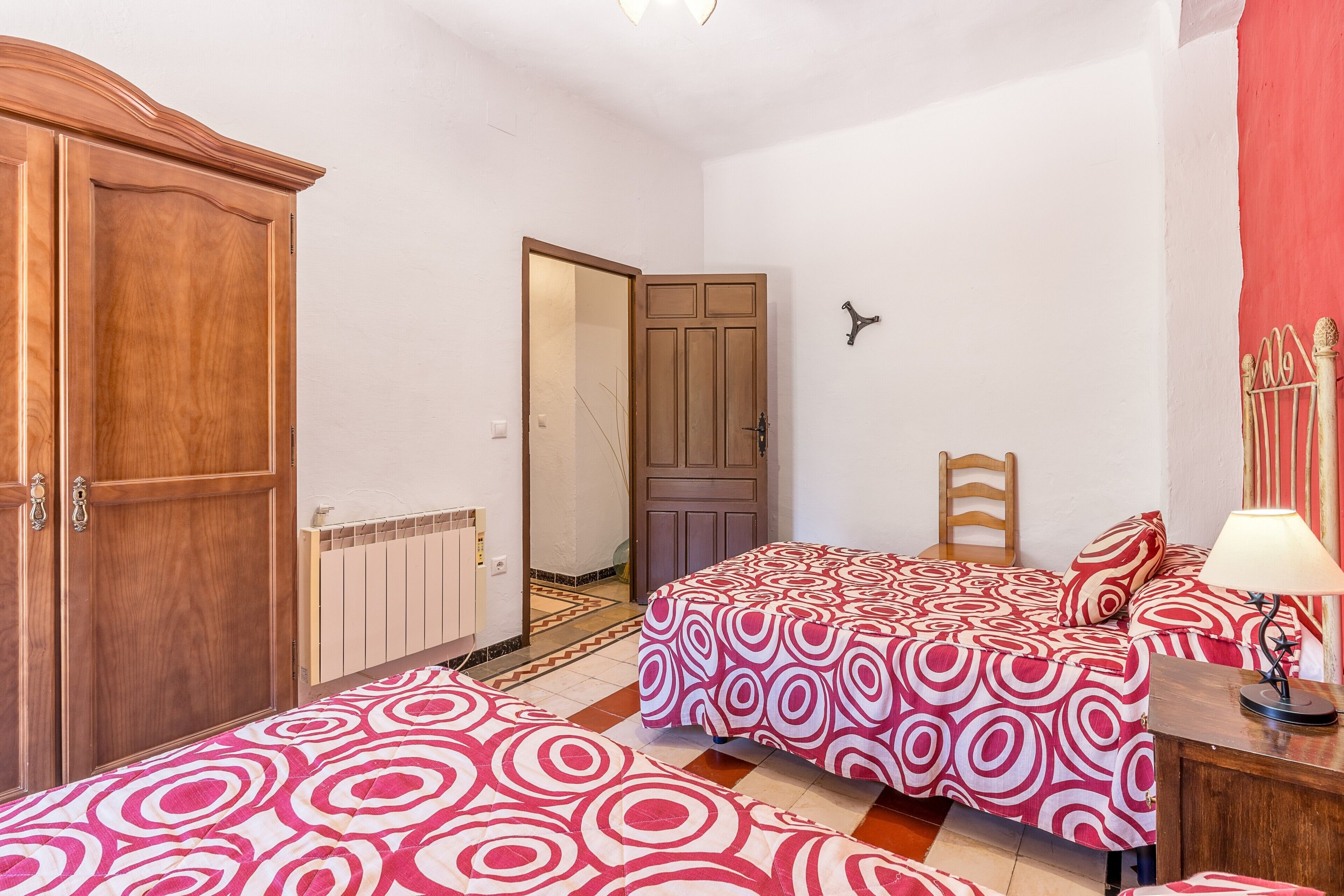 Un dormitorio con dos camas, un armario, un radiador y una puerta que da a otra habitación.