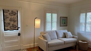 A living room with a beige sofa, a floor lamp, a wicker basket, and a door with patterned curtains.