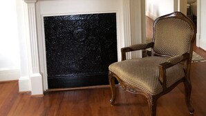 A room with a fireplace, a mirror above it, and a wicker chair in front.
