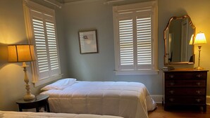 A bedroom with two beds, a dresser, a mirror, and two windows with blinds.