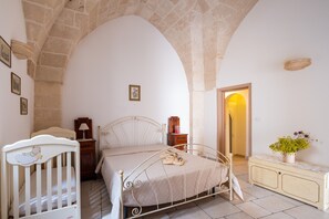 A bedroom with a bed, a crib, a nightstand, a dresser, and a mirror.