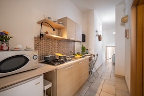 A modern kitchen with a microwave, stove, and sink. There is a wooden cabinet above the stove and a shelf with jars.