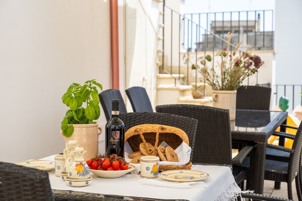 A dining table with a potted plant, a bottle, and a basket of bread.