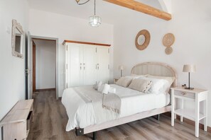 A bedroom with a bed, bedside table, wardrobe, and a hanging light fixture.