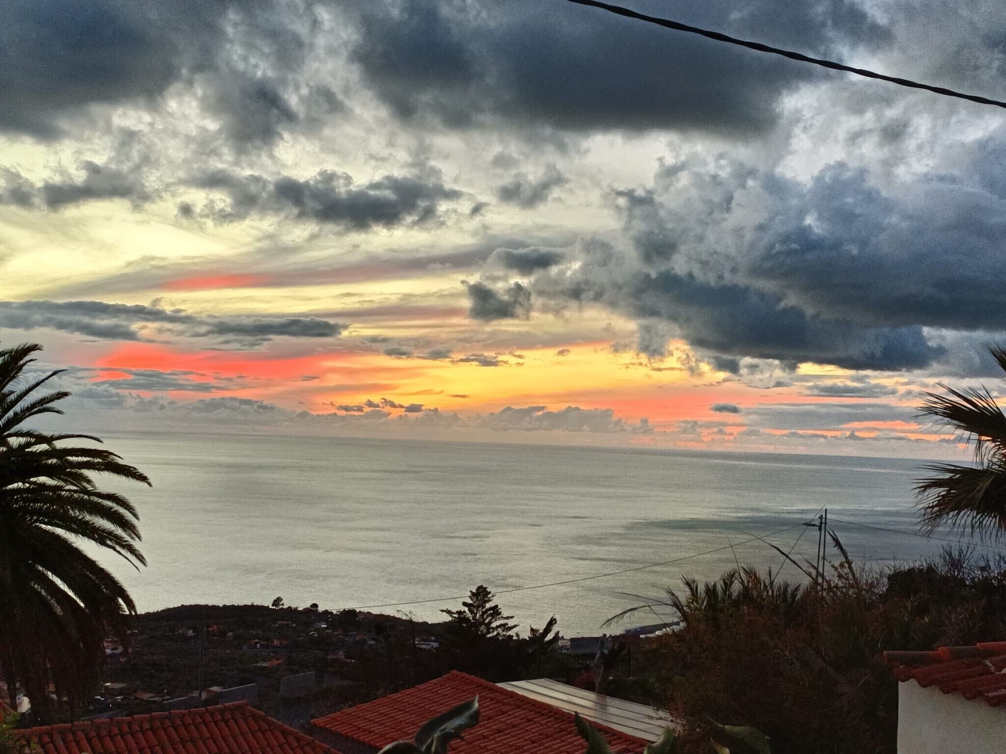 Une vue sur le coucher de soleil sur la côte, avec une maison et des palmiers.
