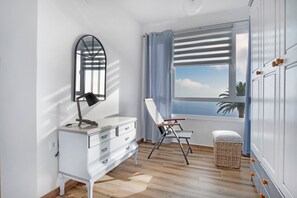 Een kamer met een witte kapstok, een spiegel, een raam met gordijnen, een stoel en een rieten mand.