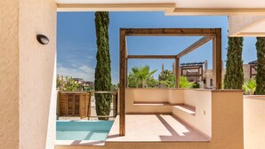 A balcony with a pool, wooden pergola, and a view of palm trees and buildings.