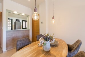 A dining area with a wooden table, chairs, a vase with flowers, and pendant lights. - Apartment 'El Oasis Martinica 8 Bajo A' with Shared Pool, Wi-Fi and Air Conditioning (Fuente Alamo)