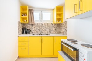 Una cocina compacta con armarios amarillos, horno empotrado y ventana con cortinas.