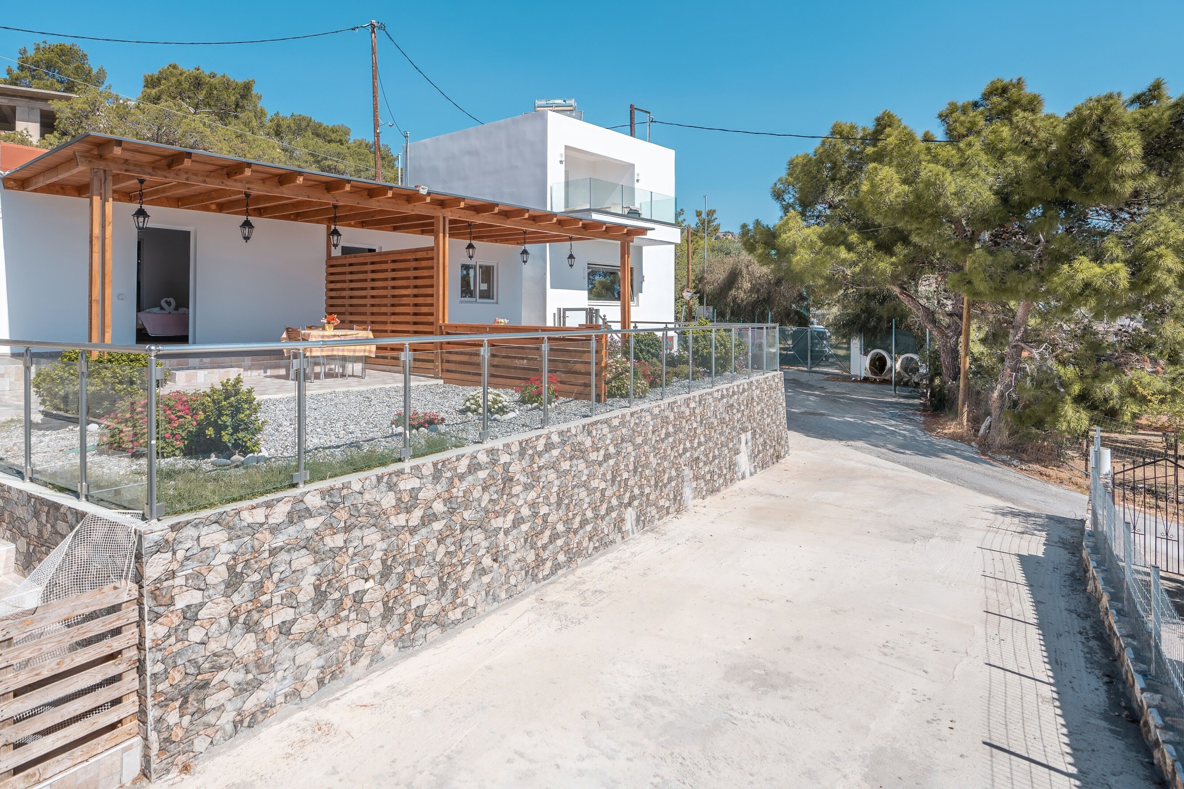 A modern house with a stone wall, a wooden pergola, and a clear view of the surrounding landscape.