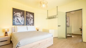 A bedroom with a bed, two wall-mounted paintings, a bedside table with a lamp, and a door leading to another room. - Apartment 'Solymar Prive  Sea View' with Sea View, Wi-Fi and Air Conditioning (Archangelos)