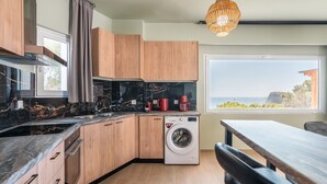 A modern kitchen with wooden cabinets, a built-in washing machine, and a dining area with a view. - Apartment 'Solymar Prive  Sea View' with Sea View, Wi-Fi and Air Conditioning (Archangelos)