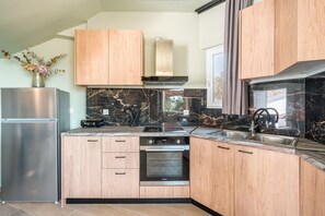 A modern kitchen with wooden cabinets, a stainless steel refrigerator, a built-in oven, and a marble backsplash.