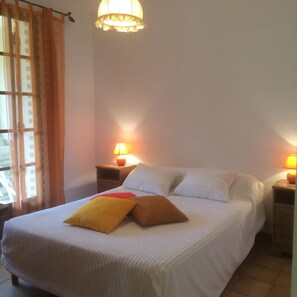 Un lit avec une literie blanche et deux oreillers, une table de chevet avec une lampe et une fenêtre avec des rideaux.