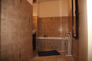 Une salle de bain avec des carreaux marron, une baignoire, un porte-serviettes blanc et un tapis foncé sur le sol.