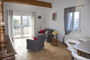 Uma sala de estar com sofá, mesa, abajur e vista para o exterior.