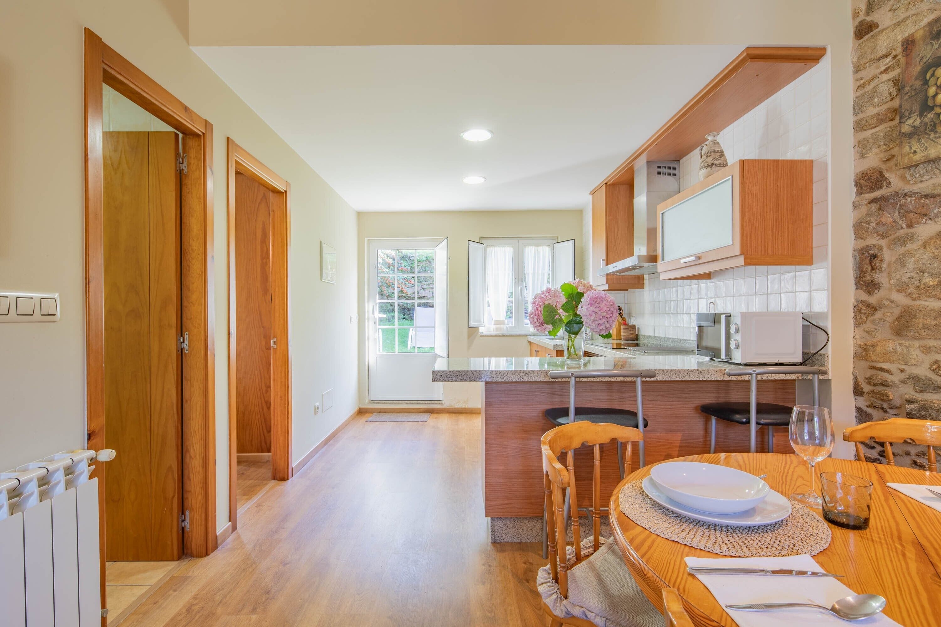 Una cocina moderna con armarios de madera, una isla central y un comedor con sillas y una mesa.