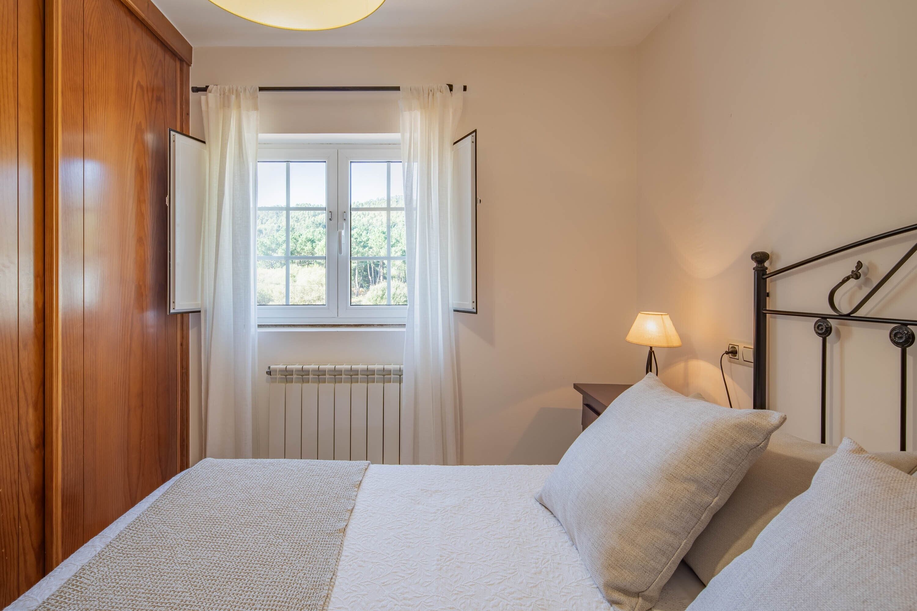Una camera da letto con un letto, un comodino, una lampada, una finestra con tende e un termosifone.