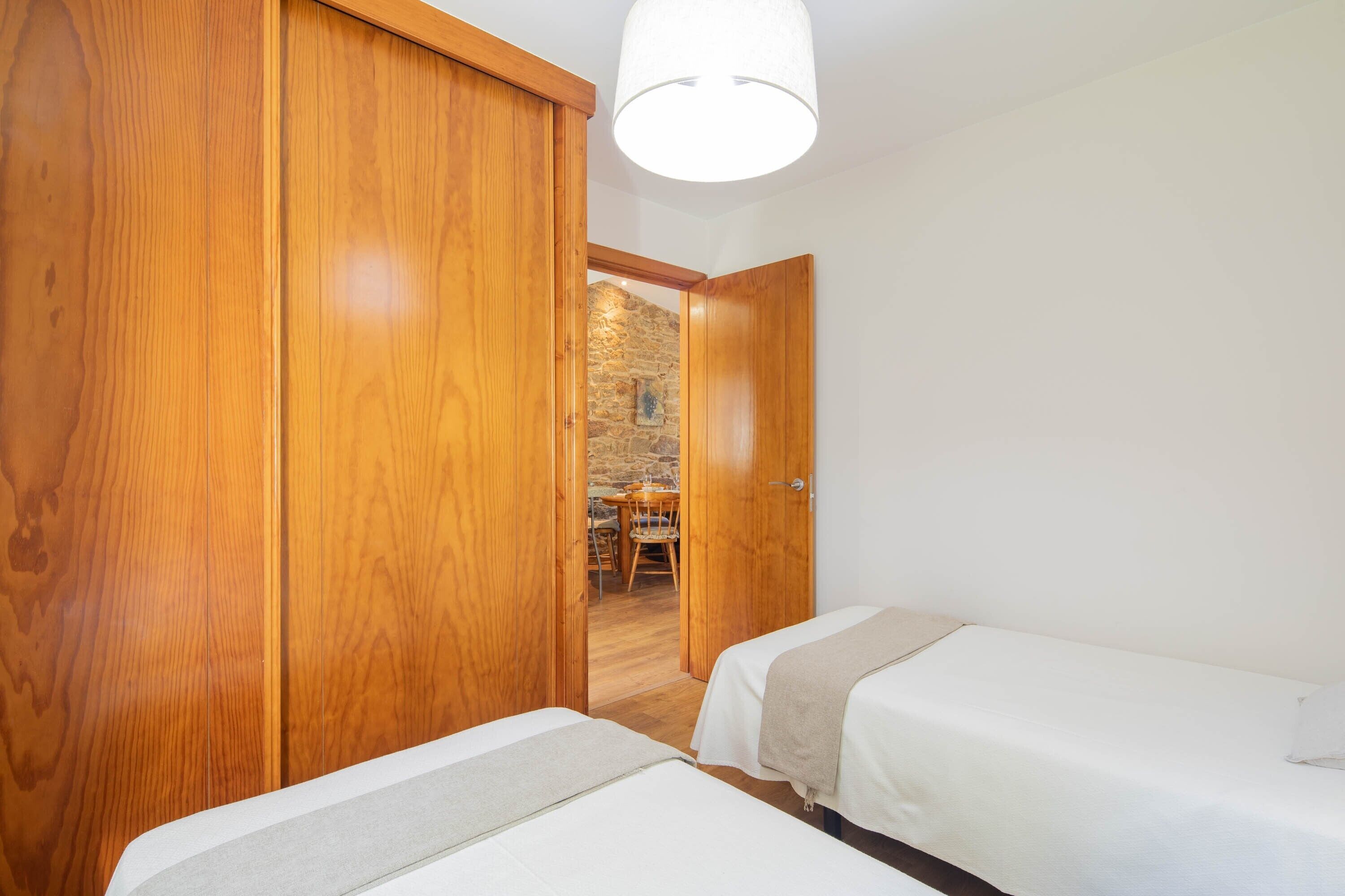 Habitación con dos camas, un armario de madera y pared de piedra visible a través de una puerta abierta.