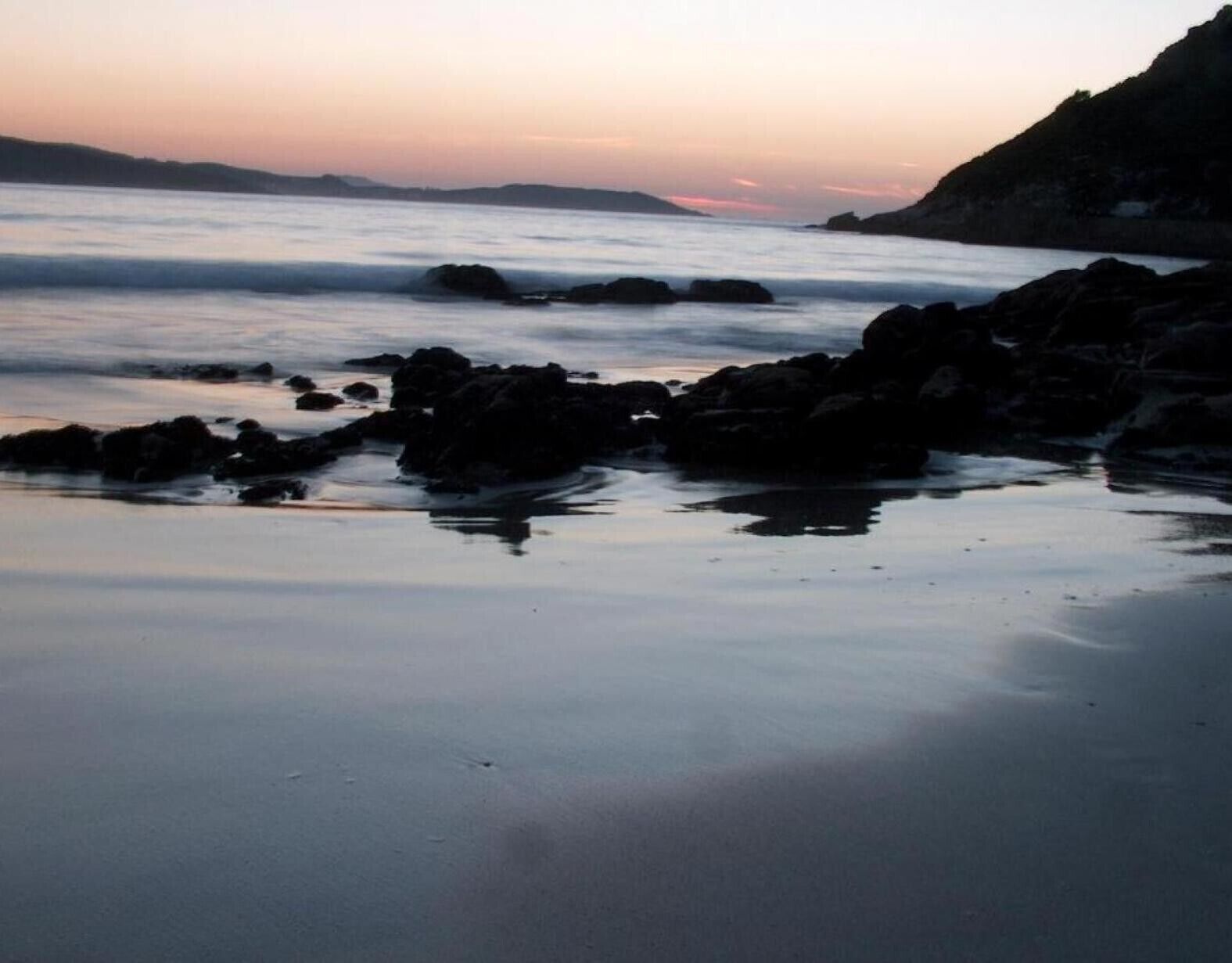 Una playa con rocas y agua tranquila.