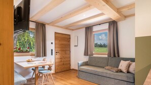 A room with a wooden ceiling, a grey sofa, a wooden dining table with chairs, and a window with curtains. - Apartment 'Larch' with Mountain View, Shared Garden and Wi-Fi (Jenesien)