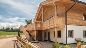 A wooden cabin with a balcony, a staircase, and a dirt path leading to the entrance. - Apartment 'Larch' with Mountain View, Shared Garden and Wi-Fi (Jenesien)