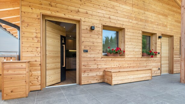 A wooden cabin with a large door, two windows with flower boxes, and a bench outside. - Apartment 'Larch' with Mountain View, Shared Garden and Wi-Fi (Jenesien)