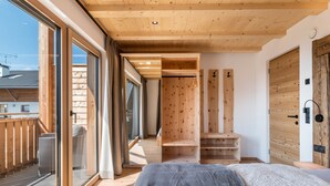 A modern bedroom with a large bed, wooden ceiling, and a sliding glass door leading to a balcony. - Apartment 'Larch' with Mountain View, Shared Garden and Wi-Fi (Jenesien)