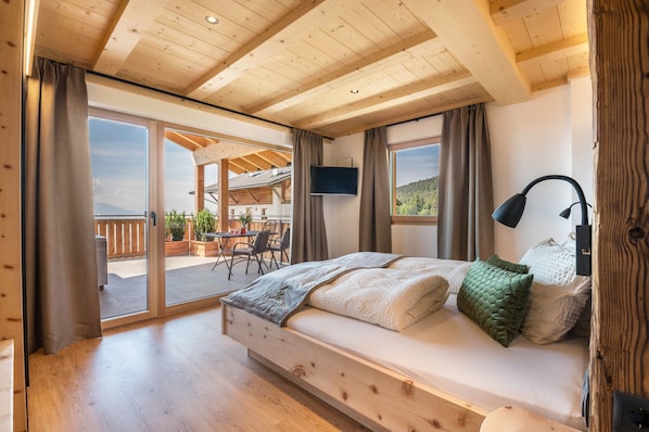 Un dormitorio con estructura de madera, una cama, un televisor y vistas al exterior.