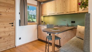 A compact kitchen with wooden cabinets, a built-in island, and a window with curtains. - Apartment 'Zirm' with Mountain View, Private Terrace and Wi-Fi (Jenesien)