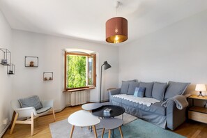 Uma sala de estar moderna com sofá, poltrona, mesa de centro, abajur e janela com vista para áreas verdes.