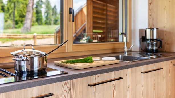 A modern kitchen with a stove, a pot, a cutting board with herbs, and a coffee maker.