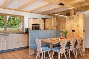 A modern kitchen with wooden cabinetry, a built-in oven, and a dining area with a bench and chairs.