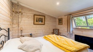 Dormitorio con paneles de madera, una cama, una araña, cuadros enmarcados y una ventana con vistas.