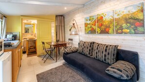 Una sala de estar acogedora con un sofá oscuro, una mesa de comedor y una zona de cocina.