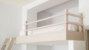 Una cama litera con escalera, paredes blancas y una puerta.