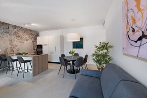 A modern kitchen with a central island, dining area with chairs, a sofa, and a large abstract painting. - Apartment 'Eleonora C3' with Shared Pool, Private Terrace, and Air Conditioning (Garda)
