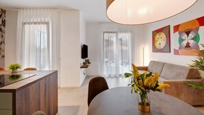 Un salon moderne comprenant un canapé, une table à manger avec des chaises, un téléviseur fixé au mur et des œuvres d’art accrochées au mur.