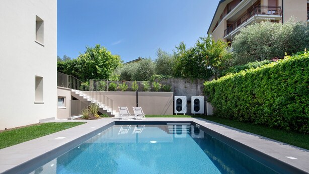 Une piscine à l’eau d’un bleu limpide, entourée d’une haie basse, avec un escalier menant à un bâtiment et deux haut-parleurs.