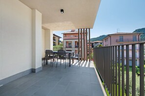 Un balcone con tavolo e sedie, vista sui palazzi circostanti e cielo sereno.